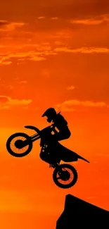 Motocross biker silhouetted against an orange sunset sky.