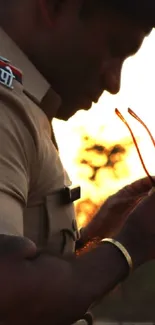 Silhouette of Indian police officer holding sunglasses at sunset.