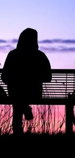 Silhouette sitting on a bench against a pink and purple sunset sky.