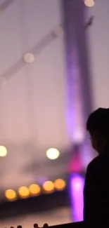 Silhouette against a vibrant, lit bridge at dusk.