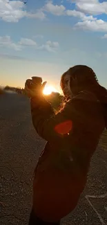 Silhouette capturing a sunset on a rural road with clouds in the sky.