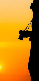 Silhouette of photographer with camera against a vibrant orange sunset.