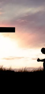 Silhouette kneeling by cross at sunset, creating a spiritual and serene atmosphere.