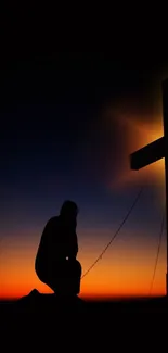 Silhouette of a person kneeling beside a cross during a beautiful sunset.