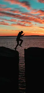 Silhouette of a person leaping across cliffs at sunset with vibrant skies.