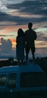 Silhouetted couple on van roof at sunset.