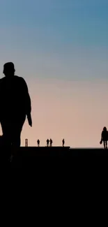 Silhouettes walking on beach at sunset beneath sky blue gradient.