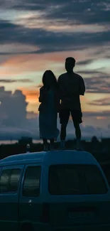 Silhouette of couple on van roof against sunset sky.