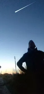 Silhouette under a nighttime sky with a bright meteor streak.