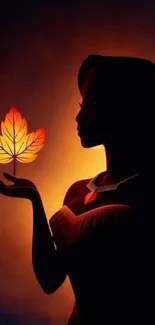 Silhouette holding a vibrant autumn leaf against a dark orange background.