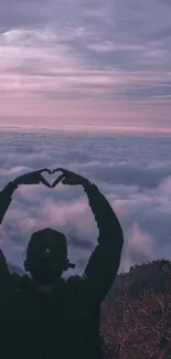 Silhouette making heart shape against purple sunset clouds.