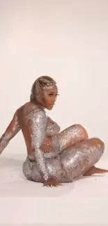 Model covered in silver glitter sitting on a neutral background.