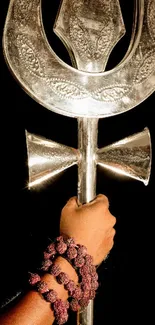 Silver trident against a dark background with a decorative handle.