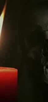 A red candle illuminating a skull in the dark.