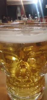 A skull-shaped beer mug filled with golden ale on a table.