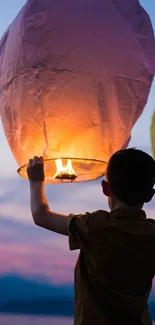 Child releasing a glowing lantern at sunset.