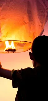 Child releasing an orange glowing lantern at sunset.