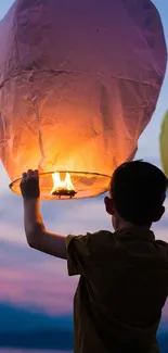 Boy holding a glowing sky lantern during a festival evening.