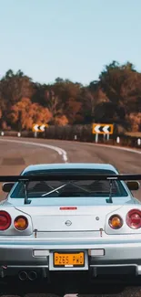 Silver Nissan Skyline on a scenic winding road with autumn trees.