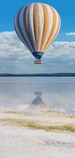 Hot air balloon floats over calm waters with blue sky backdrop and cloud reflection.