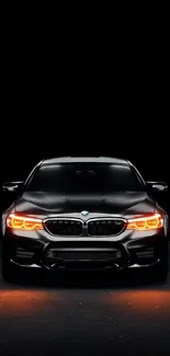 Sleek black car with glowing headlights at night in high-resolution wallpaper.