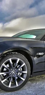 Sleek black car on a snowy road with dynamic sky.
