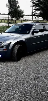 Elegant black sedan on gravel road with trees in background.