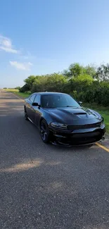 Sleek black car on an open road under a blue sky.