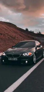 Sleek black car on an open road at sunset with brown sky.