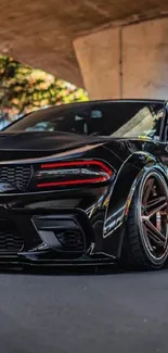 Sleek black sports car under urban bridge.