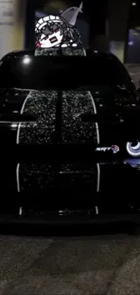 Sleek black muscle car at night with bright headlights.