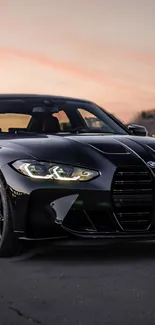 Sleek black car with glowing headlights against sunset sky.