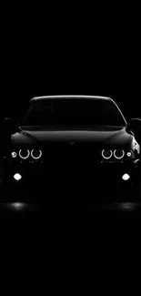 Front view of a sleek black car with glowing headlights in the dark.