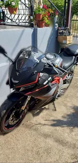 Sleek black motorcycle under sunlight near a house with potted plants and rail.