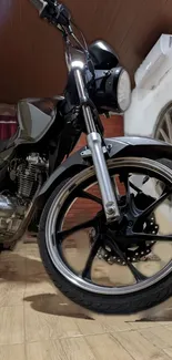 Sleek black motorcycle in rustic indoor setting with focus on wheels.