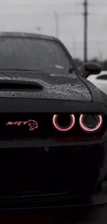 Sleek black muscle car with pink headlights on a rainy day.