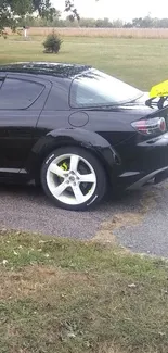 Black sports car with yellow spoiler and white rims parked on a road.