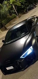 Sleek black sports car parked under streetlights at night.