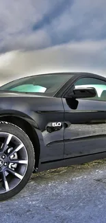 Sleek black sports car on snowy terrain under cloudy sky.