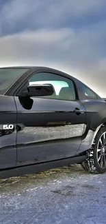 Sleek black sports car parked on snowy ground under a cloudy sky.