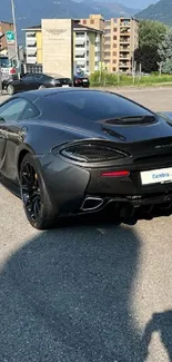 Sleek black sports car parked by a glass building with scenic mountain view.