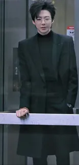 Stylish person in black suit behind glass panel.