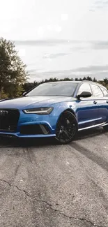 Sleek blue car on an open road with scenic trees in the background.