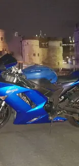 Blue motorcycle in front of historic city at night.