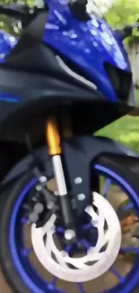 Close-up of sleek blue motorcycle front wheel under greenery.