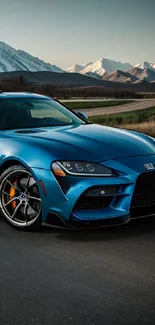 Sleek blue sports car on road with scenic mountain background.