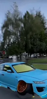 Blue sports car parked on urban street with trees in background.