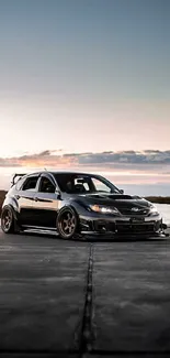 Sleek black car on road with sunset backdrop.