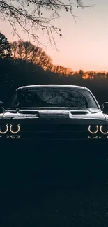 Car silhouette at sunset with glowing headlights in scenic wallpaper.