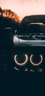 Sleek car at dusk with glowing headlights and a sunset backdrop.